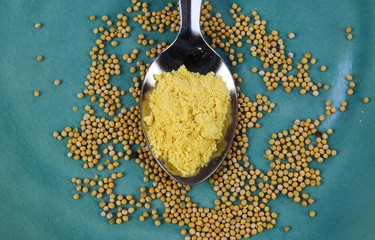 Close up of isolated silver spoon with yellow mustard powder and raw seeds on blue old scratched...