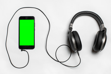 Obraz premium black phone with green screen and headphones on white background, view from above