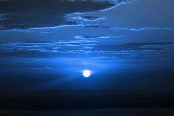 Sunset sky. Toned classic blue. Clouds and bright sunny circle over dark foggy landscape.