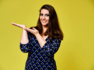 Portrait of a pretty brunette woman with a beautiful hairstyle and with excellent makeup in a dark blue blouse on a yellow background. It stands showing hands with a smile in front of the camera.