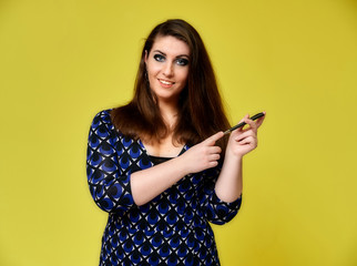 Portrait of a pretty brunette woman with a beautiful hairstyle and with excellent makeup in a dark blue blouse on a yellow background. He stands with a smile and shows with his hands.