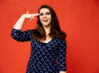 Fototapeta premium Portrait of a pretty brunette woman with a beautiful hairstyle and with excellent makeup in a dark blue blouse on a red background. He stands with a smile and shows his hands with emotions.