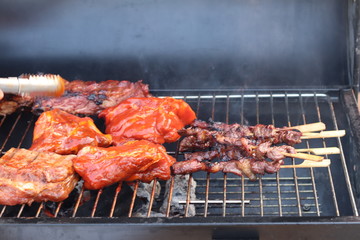 Assorted delicious grilled meat with beef stick and beef steak on black stove with smoke. grills some kind of marinated meat and vegetable on gas grill during summer party time. 