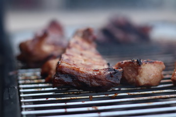 Assorted delicious grilled meat with beef stick and beef steak on black stove with smoke. grills some kind of marinated meat and vegetable on gas grill during summer party time. 