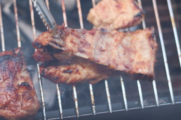 Assorted delicious grilled meat with beef stick and beef steak on black stove with smoke. grills some kind of marinated meat and vegetable on gas grill during summer party time. 