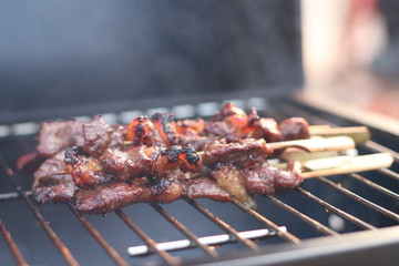 Assorted delicious grilled meat with beef stick and beef steak on black stove with smoke. grills some kind of marinated meat and vegetable on gas grill during summer party time. 
