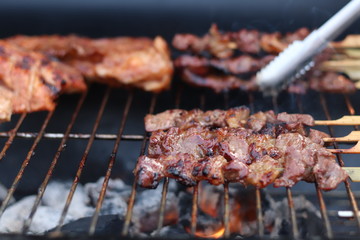 Assorted delicious grilled meat with beef stick and beef steak on black stove with smoke. grills some kind of marinated meat and vegetable on gas grill during summer party time. 