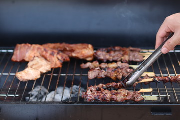 Assorted delicious grilled meat with beef stick and beef steak on black stove with smoke. grills some kind of marinated meat and vegetable on gas grill during summer party time. 