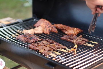 Assorted delicious grilled meat with beef stick and beef steak on black stove with smoke. grills some kind of marinated meat and vegetable on gas grill during summer party time. 