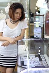 Fototapeta na wymiar Asian short hair woman which is customer choosing and looking for jewellery gift for her special day with happy face. woman wearing beautiful natural pearl necklace in jewellery store