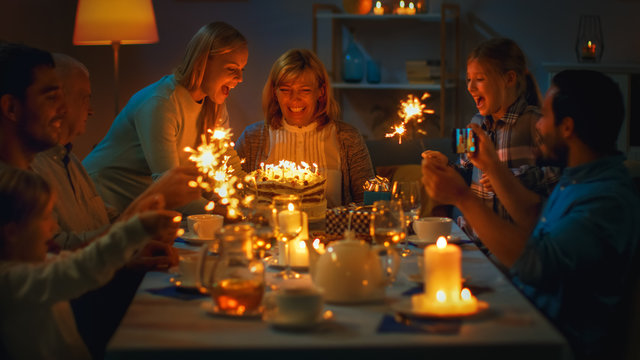 Shot of a Daughter Bringing Birtday Cake with Candlelights to Her Senior Mother. Family Dinner and Celebration, People Gathered at the Evening Dinner Table.