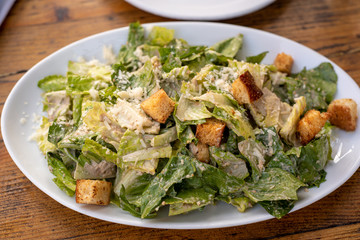 Top view of healthy organic Cezar salad on white plate on wooden background, cropped, dinner angle view