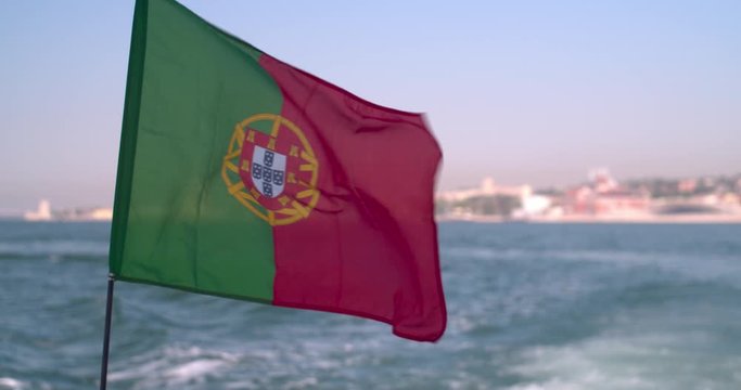 Portuguese flag waving at the wind on a boat . Slow motion shot with Lisbon cityscape on the background.