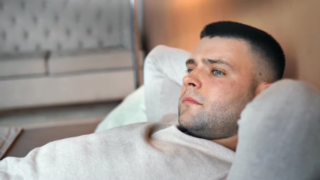 Close-up face of pensive handsome young brown guy lying on bed dreaming and relaxing