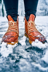 Feet of a woman on a snowy sidewalk in brown boots. Winter slippery pawement. Seasonal weather...