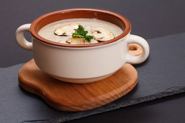 Cream soup with mushrooms in porcelain bowl on black background.