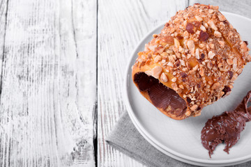 Trdelnik covered in nuts and sugar with chocolate inside against white wooden background. Czech street food