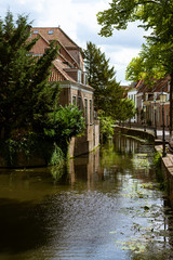 Fototapeta na wymiar Beautiful and picturesque landscape of the village of Amersfoort, the Netherlands. Typical dutch houses in front of a canal, riverside with trees and flowers. A sunny day.