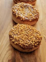Three salted caramel doughnut with golden crumb on a wooden board and table.