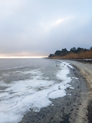 Beach with frozen water at the shore. Winter seascape with dark cloudy sky and a little sunlight in the horizon. Sæby, denmark.