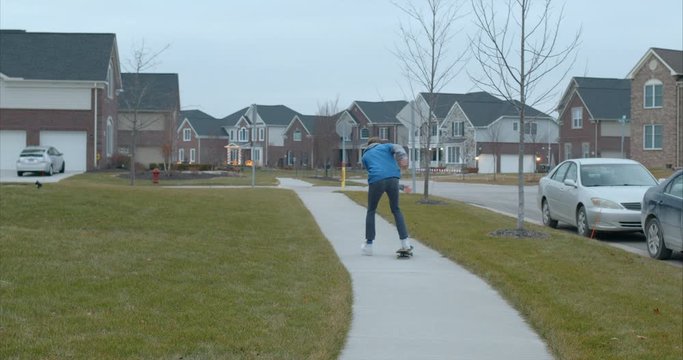 teen boy skateboards down the sidewalk away from the camera