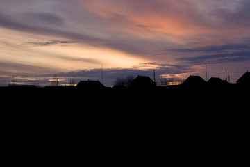 Obraz premium The silhouette of houses and roofs against the sunset. Rural houses and trees on the background of a colorful gorgeous sunset.