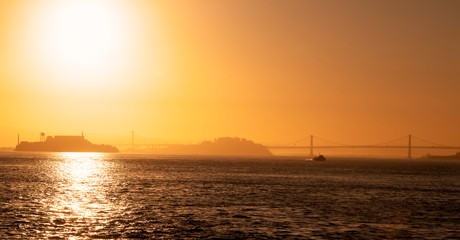 Naklejka na ściany i meble Early morning in the San Francisco Bay with Alcatraz Island , Bay Bridge and Treasure Island in silhouette with a fishing boat heading out to sea