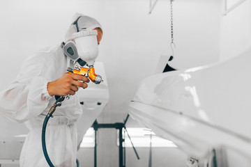 Worker in protective workwear painting car parts using spray compressor.