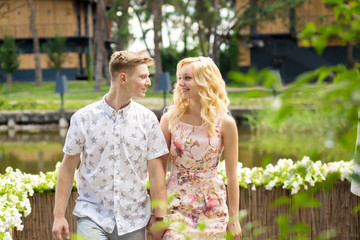 Young charming blonde girl is flirting and with a guy in the garden. Lovestory of a couple in love