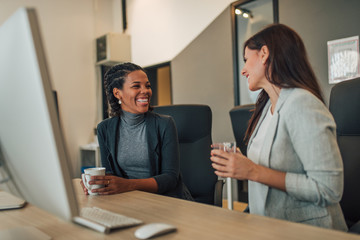 Two female coworkers having fun talking in the office.