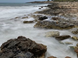 Fototapeta na wymiar Long exposure of waves against coast line rocks with blue sea and sky background