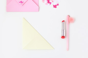 Flat lay: pink envelope, lipstick, pen, confetti hearts, yellow paper folded in the shape of heart in the origami technique. Making postcard for Valentine's Day. Do it yourself. Photo from the series