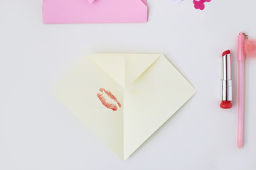 Flat lay: pink envelope, lipstick, pen, confetti hearts, yellow paper folded in the shape of heart in the origami technique. Making postcard for Valentine's Day. Do it yourself. Photo from the series