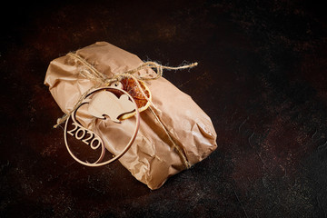 on a dark textural background a gift bundle made of Kraft paper tied with twine with the emblem of the new year symbol mouse made of plywood