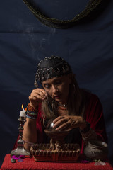 Gypsy fortuneteller or esoteric Oracle holding a smoking piece of wood and a magic crystal ball