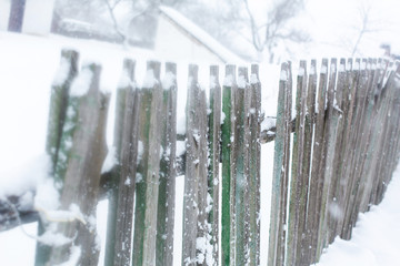 Winter old dilapidated rickety fence of wooden boards. A snow blizzard.