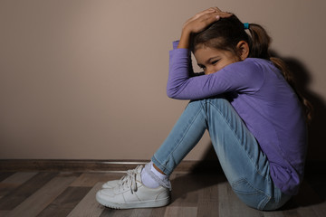 Scared little girl near beige wall, space for text. Domestic violence concept
