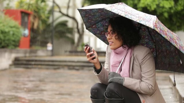 Latin girl with brunette skin and curly hair, in the rain, enjoying the moment, answering the phone and smiling at life