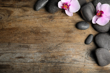 Fototapeta na wymiar Stones with orchid flowers and space for text on wooden background, flat lay. Zen lifestyle