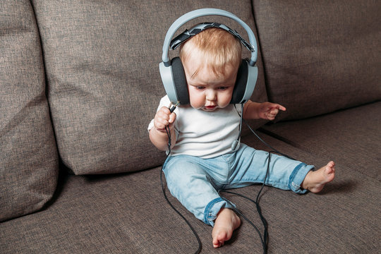 little child listening music with headphones on his head sitting on sofa at home