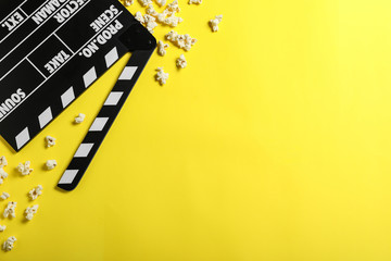 Clapper board and popcorn on yellow background, flat lay with space for text. Visiting cinema