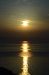 Highly bright sun over the calm sea, adorned with a long&wide solar track on slightly rippled water. Contrast seascape: a glowing sun behind the rare light clouds, above the deeply shadowed horizon