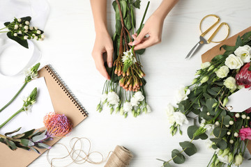 Florist making beautiful bouquet at white wooden table, top view