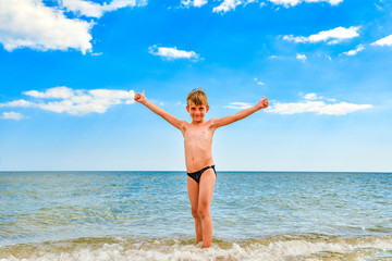 Fototapeta na wymiar A boy at the sea stands on the beach with his arms outstretched to the sides.