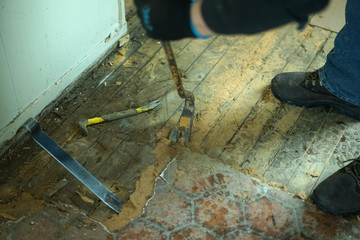 Worker demolishing old floor with crowbar tool.