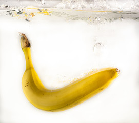 one banana falls into the water with splashes and bubbles on a white background