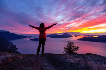 Fototapeta na wymiar Adventurous Caucasian Girl standing on top of a mountain during a colorful winter sunset. Taken on Tunnel Bluffs Hike, North of Vancouver, BC, Canada.