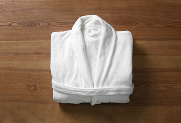 Clean folded bathrobe on wooden background, top view