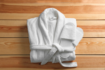 Clean folded bathrobe and slippers on wooden background, top view