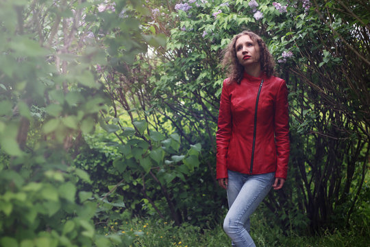 Outdoors portrait of a pensive girl in a red jacket, close-up, in park. Real people
